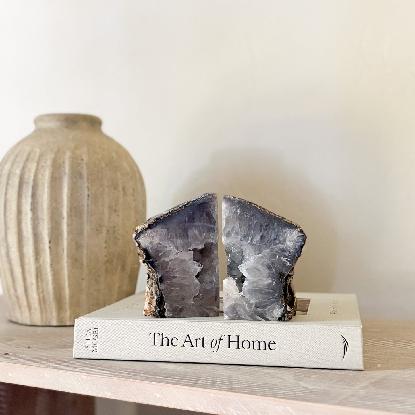 Geode bookends on a book titled 'The Art of Home' with a vase in the background.