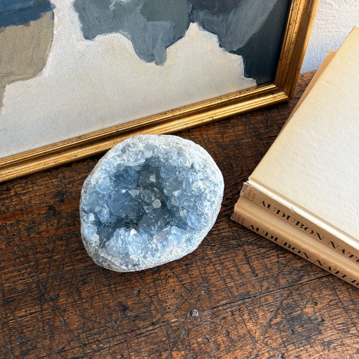 blue Geode crystal on a wooden surface with books and a framed picture in the background