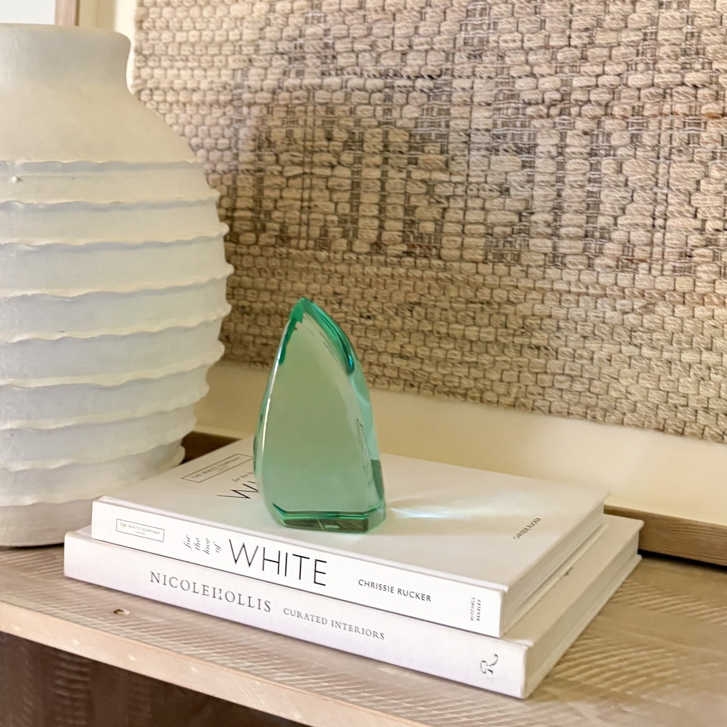 Modern green glass art piece resting on stacked interior design books beside a textured white vase