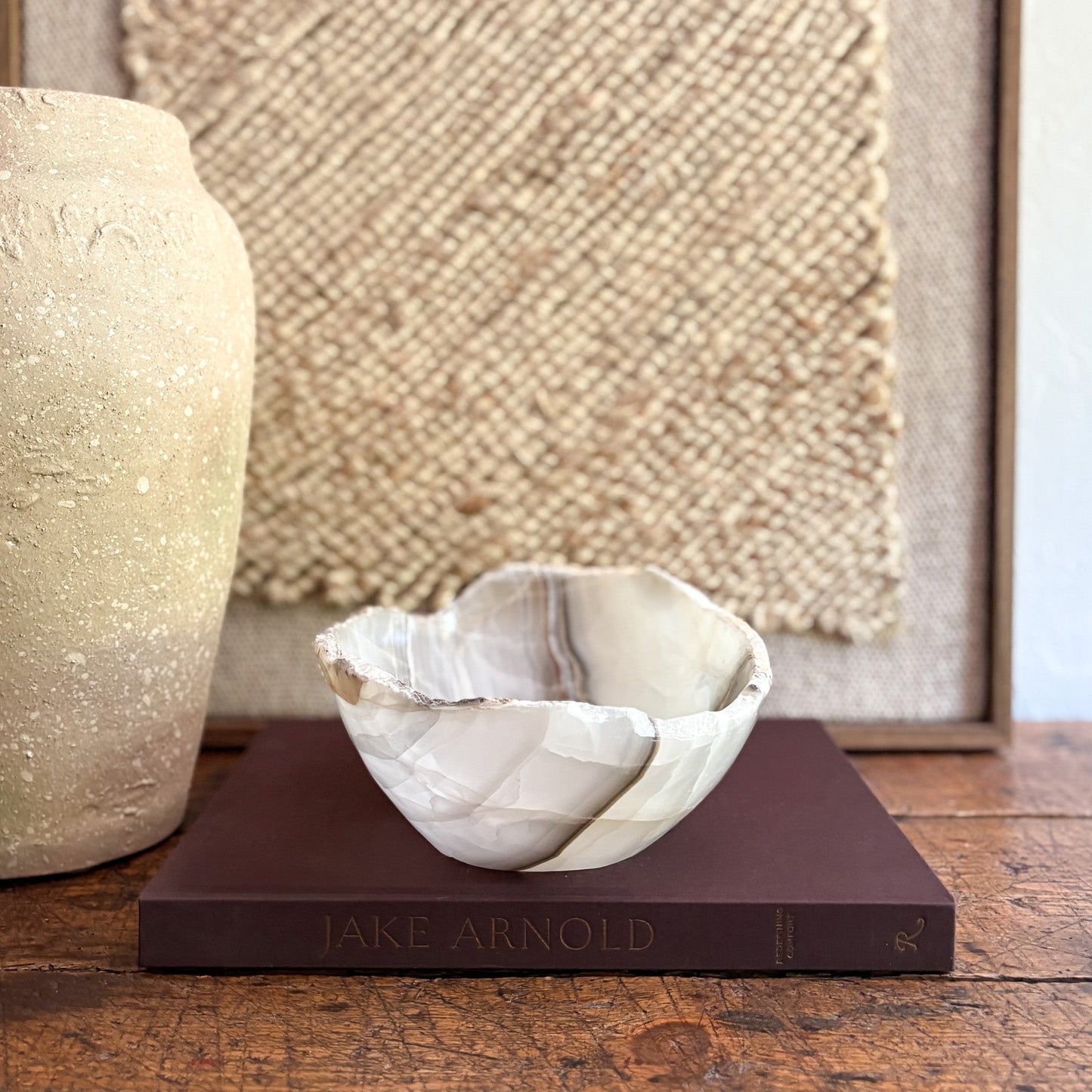 Decorative onyx bowl on a book with a textured wall and vase in the background