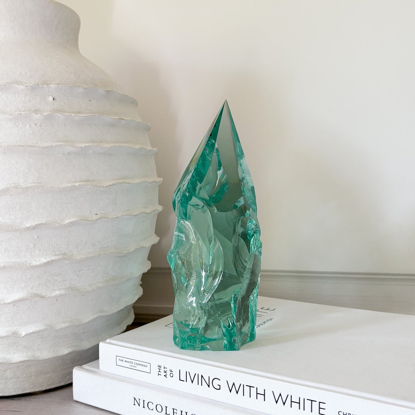 Teal glass sculpture on a stack of books with a white textured vase in the background