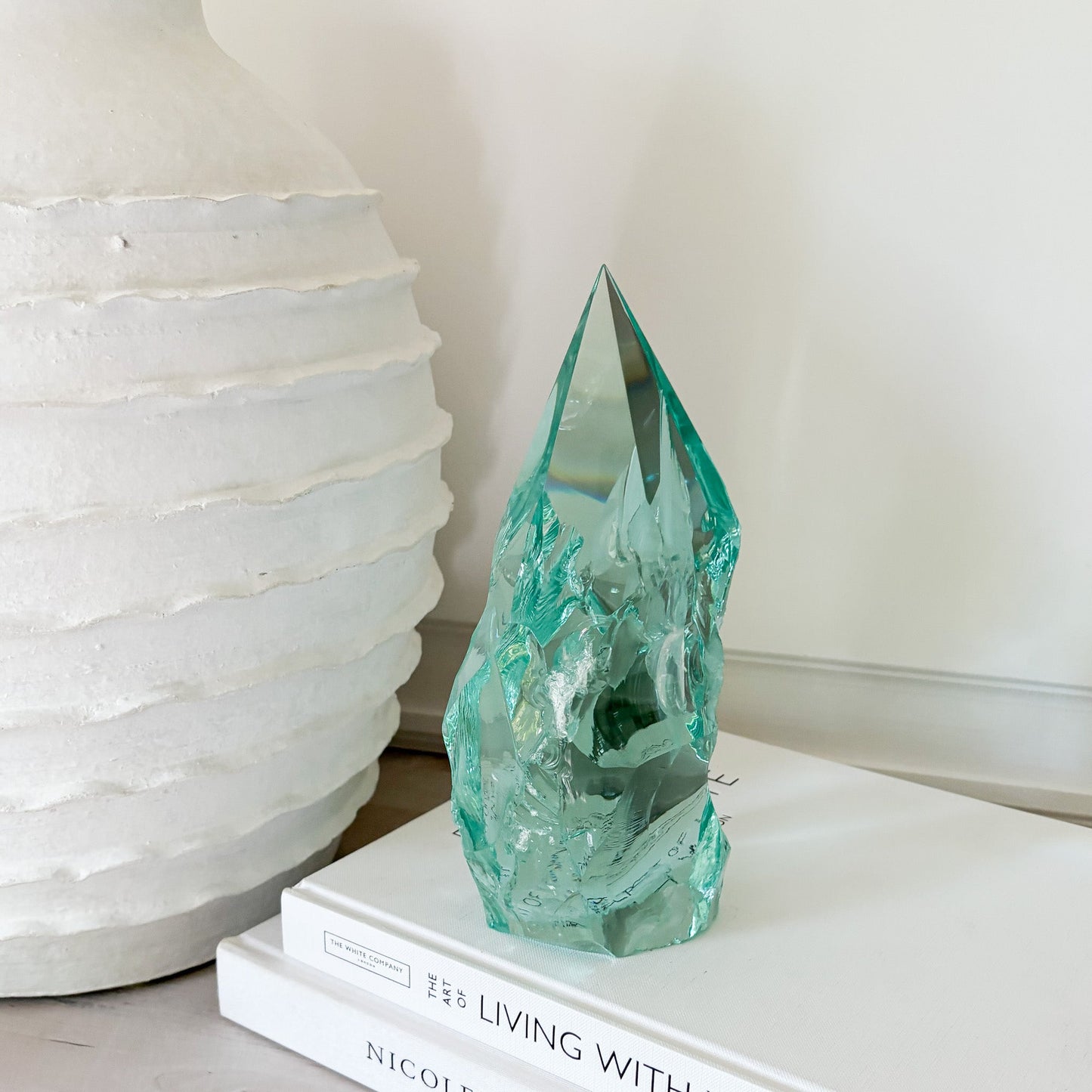 Green crystal sculpture on a stack of books with a white textured lamp in the background