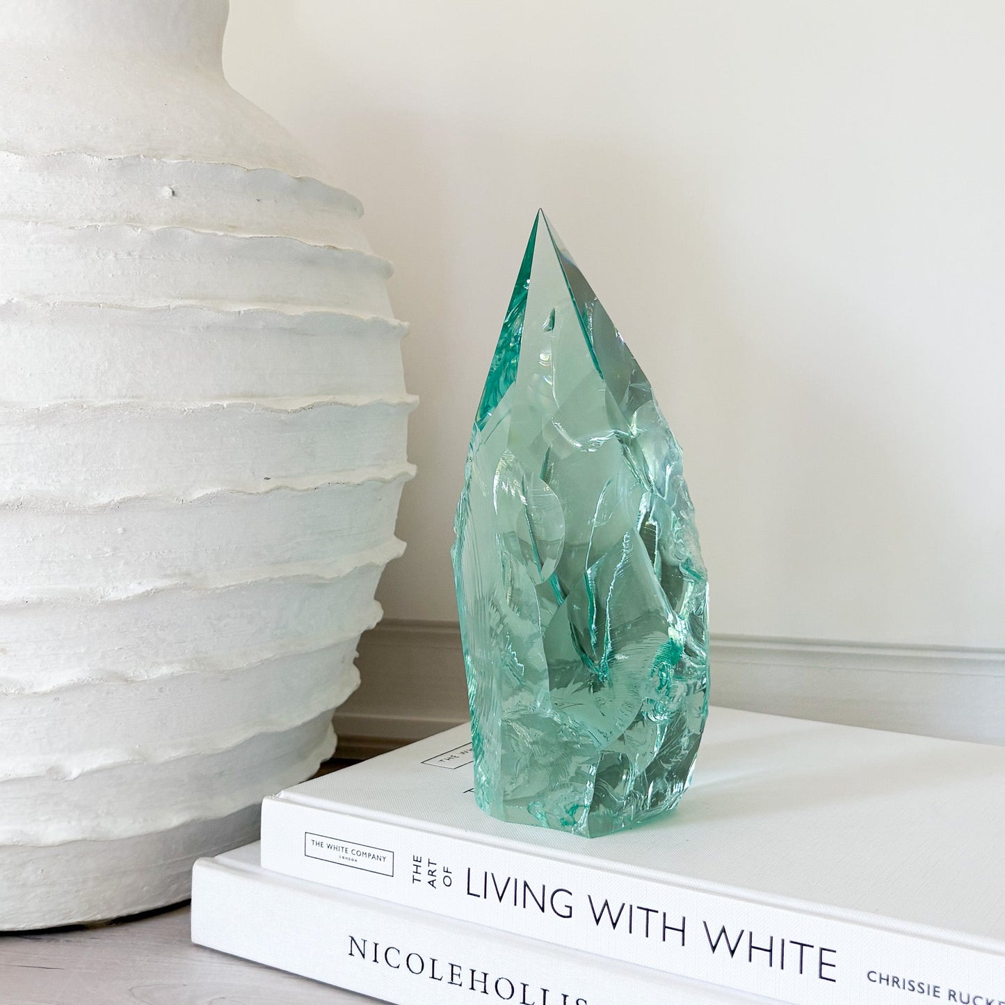 Green glass sculpture on a stack of books with a white textured vase in the background