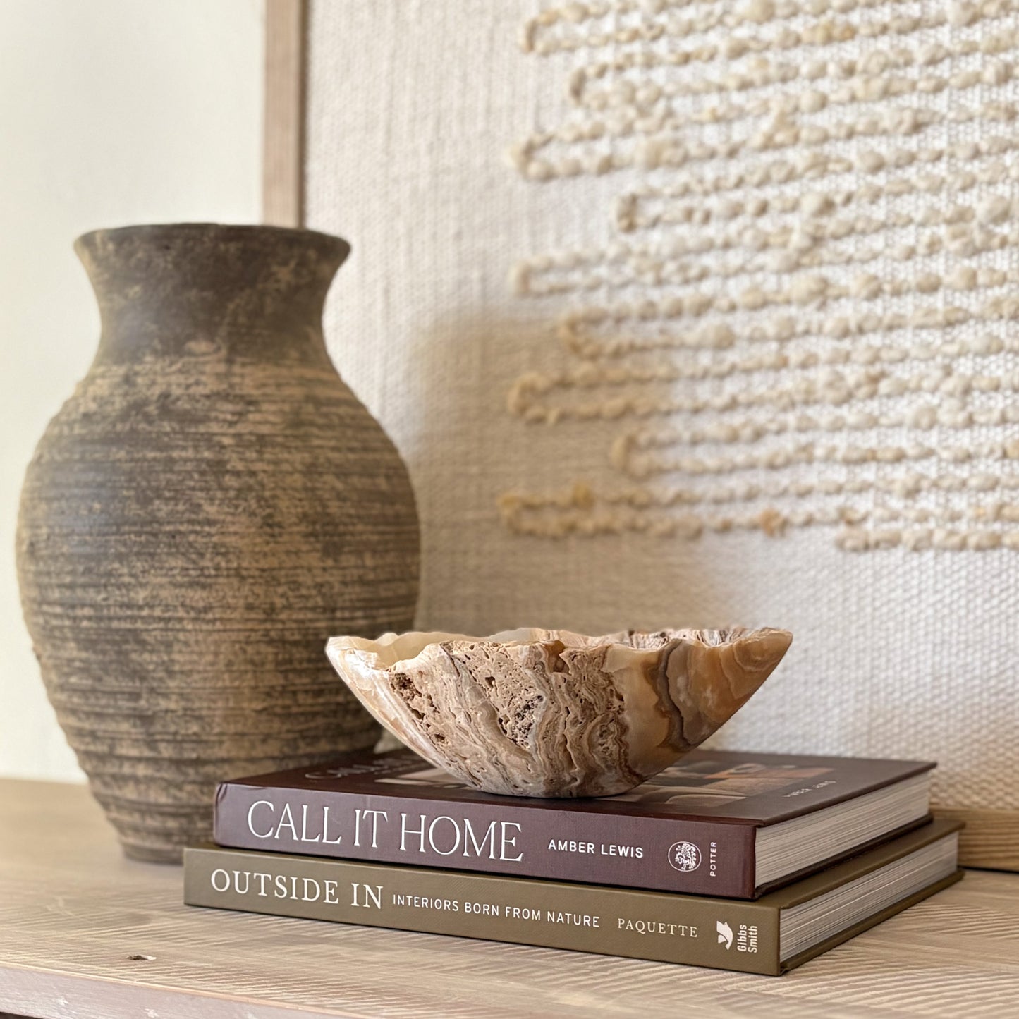 Small hand-carved amber onyx bowl displayed on stacked coffee table books in a neutral home décor setting