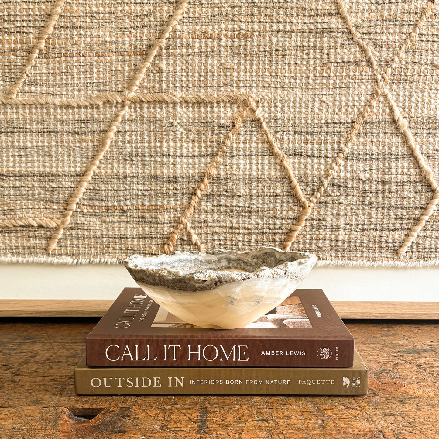 Stack of books titled 'Call It Home' and 'Outside In' with a decorative onyx bowl on top, against a textured wall.