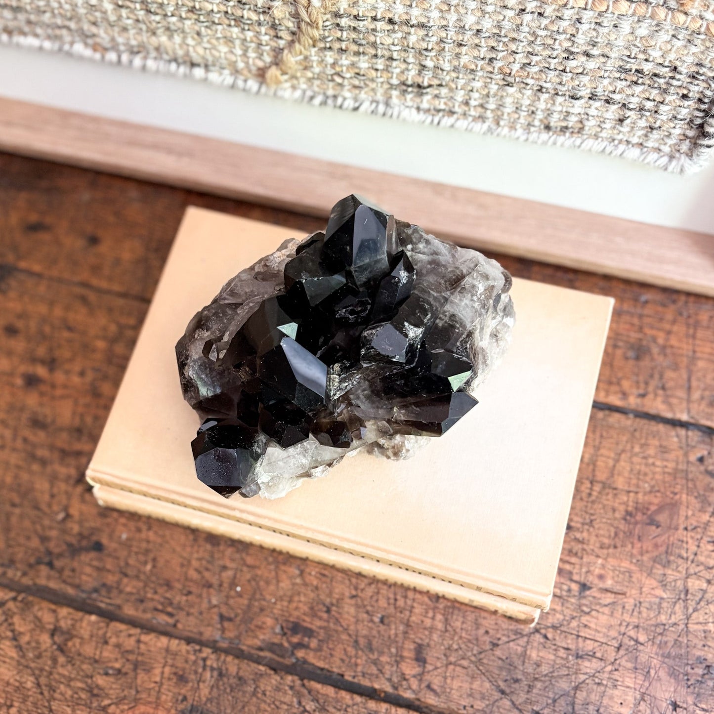dark quartz crystal mineral specimen on a wooden block with a textured fabric background