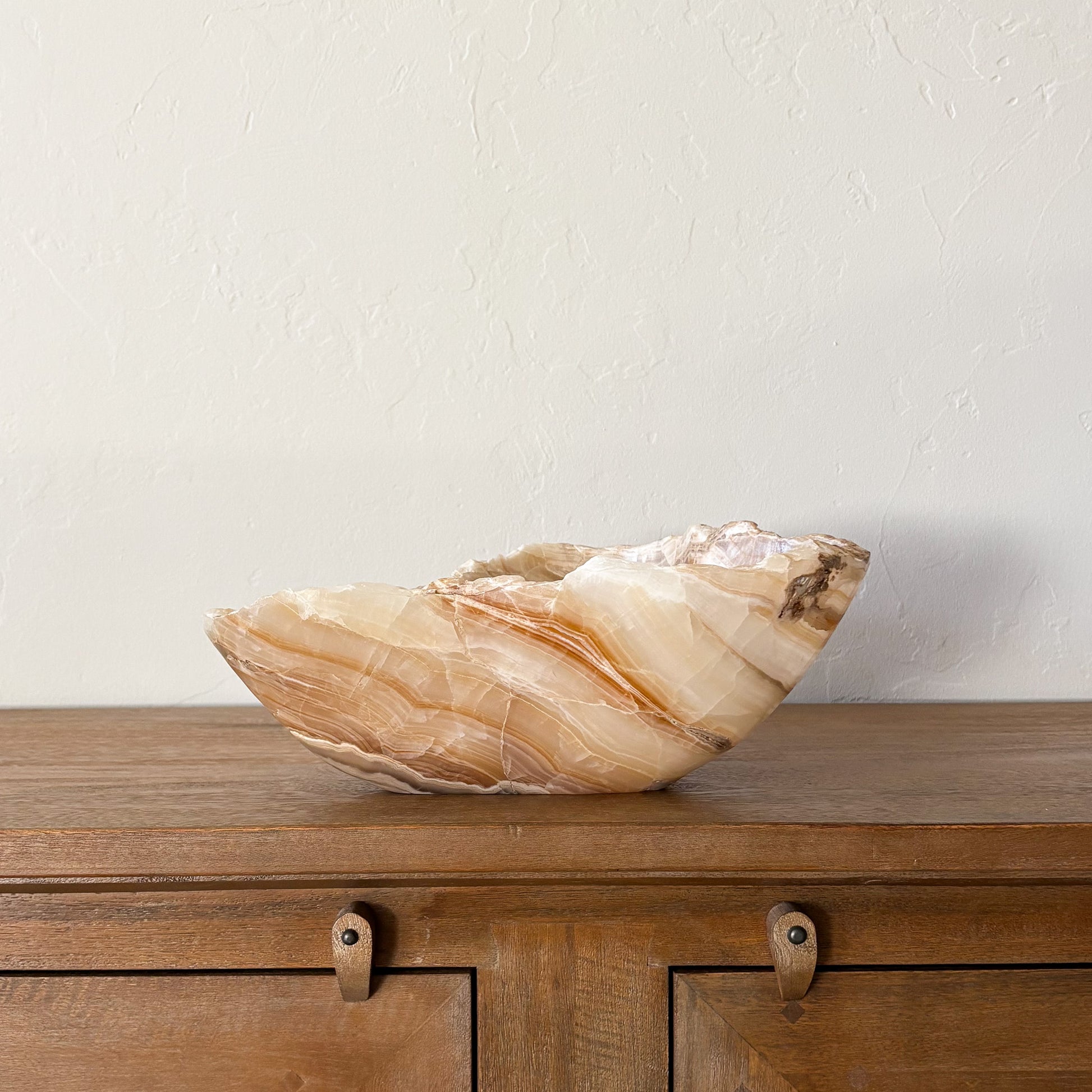 Large hand carved amber onyx bowl with natural banded stone pattern on wooden console table