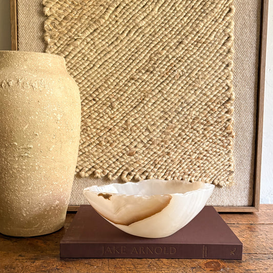 Decorative white and brown bowl on a book with a textured wall in the background