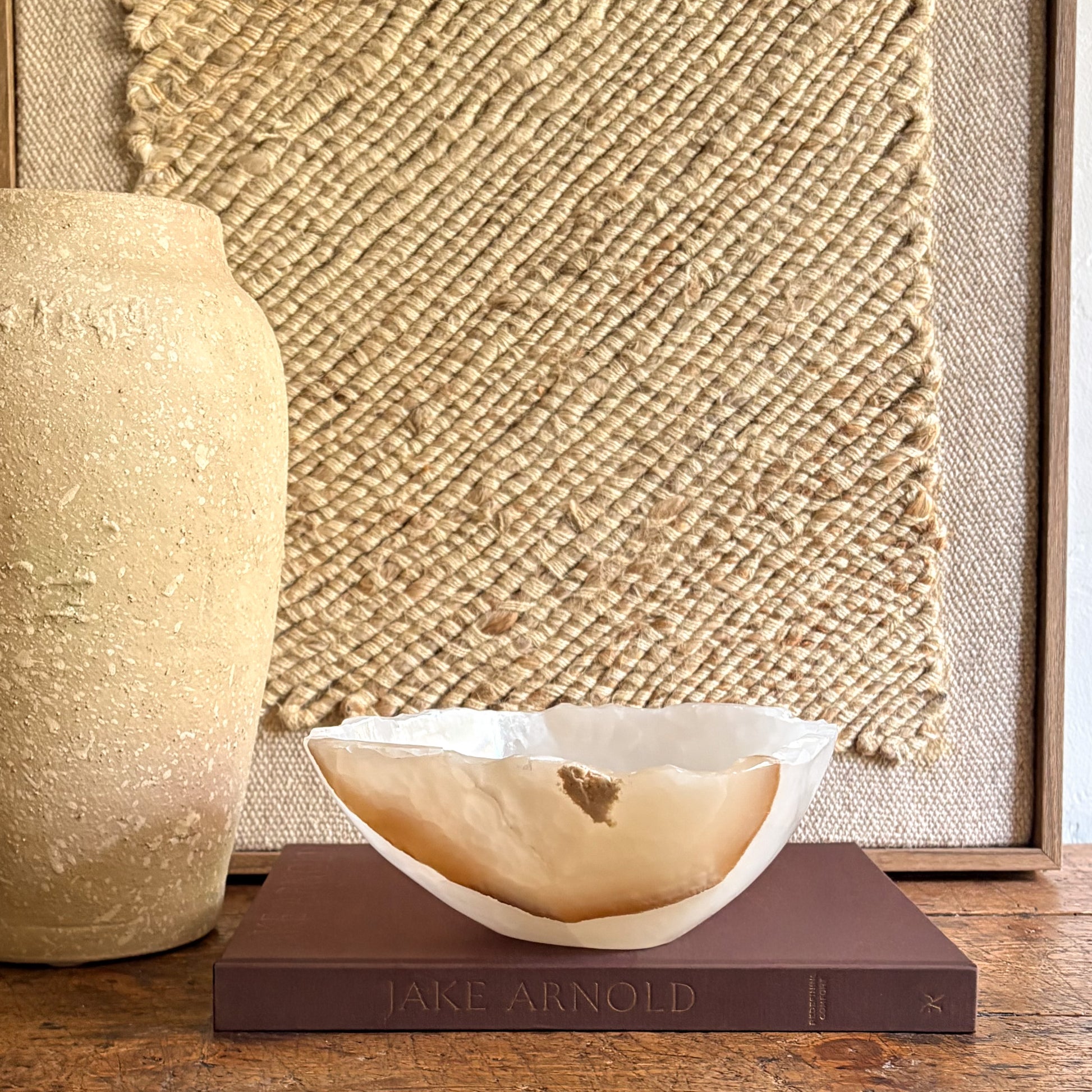 Decorative white and brown stone bowl on a book with a textured wall in the background