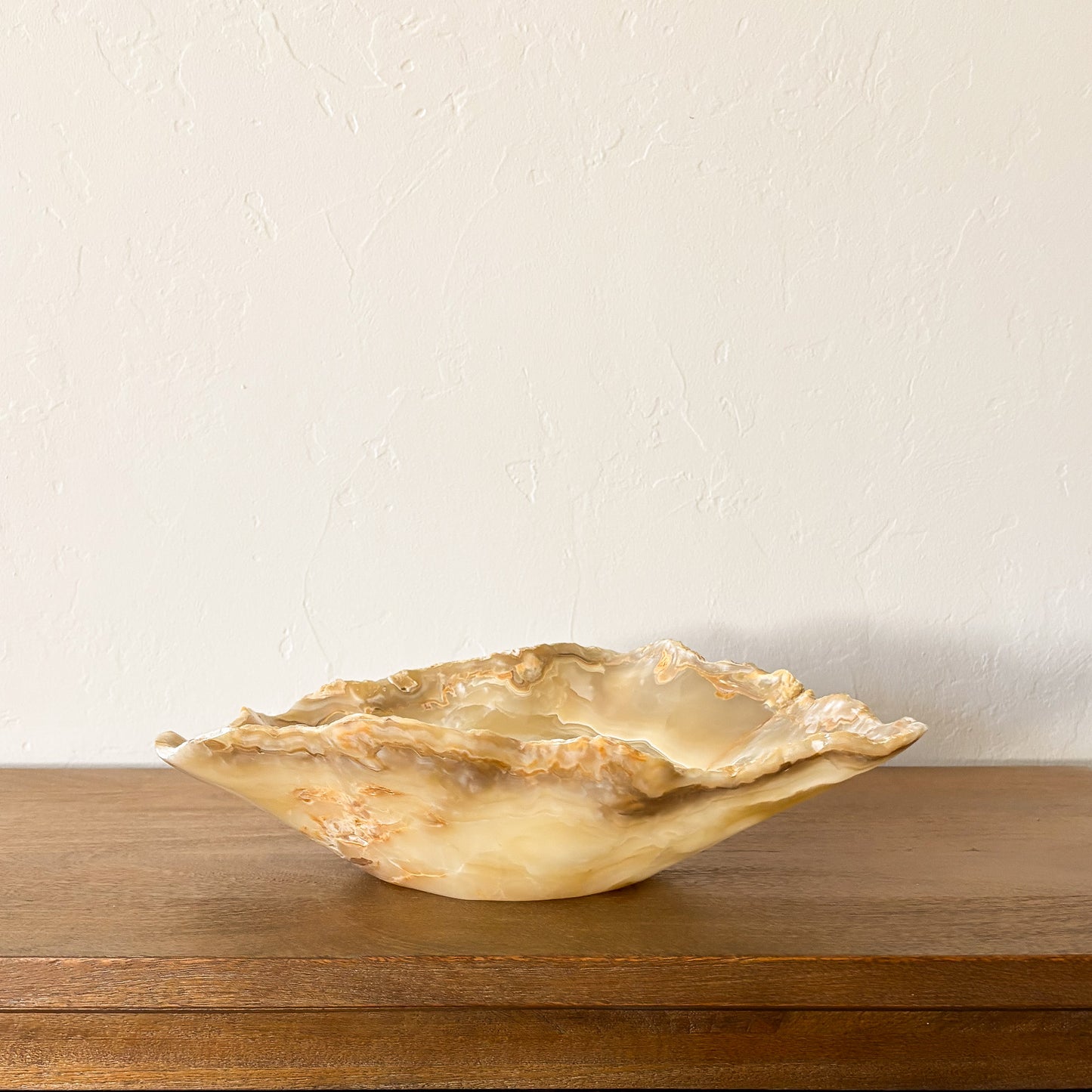 Large hand carved amber onyx bowl with natural banded stone patterns displayed on wooden table