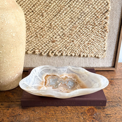 Decorative brown and white stone bowl on a book with a textured wall in the background