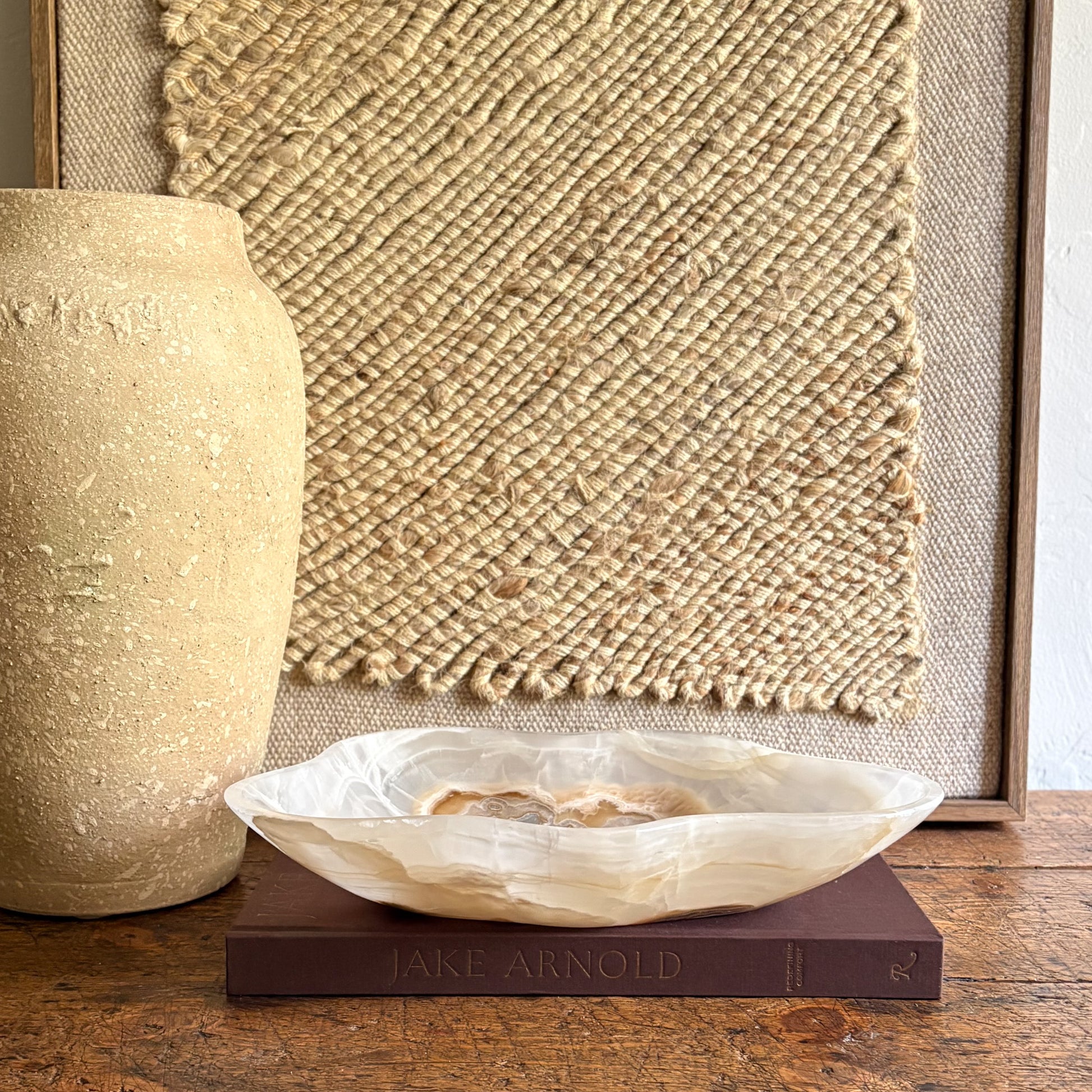 Decorative onyx stone bowl on a book with a textured wall and vase in the background