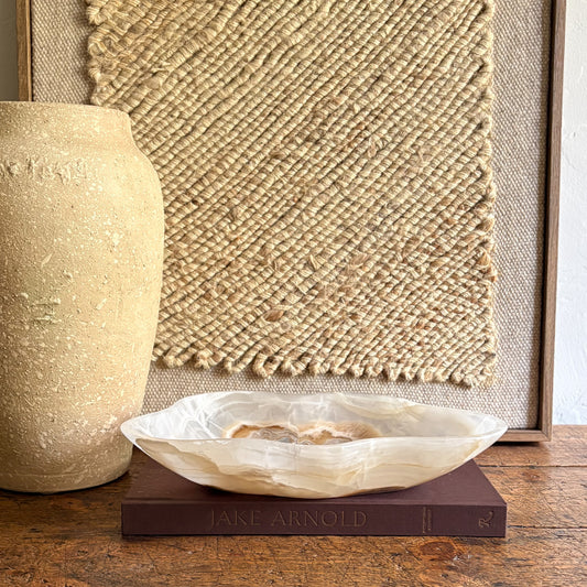 Decorative onyx stone bowl on a book with a textured wall and vase in the background