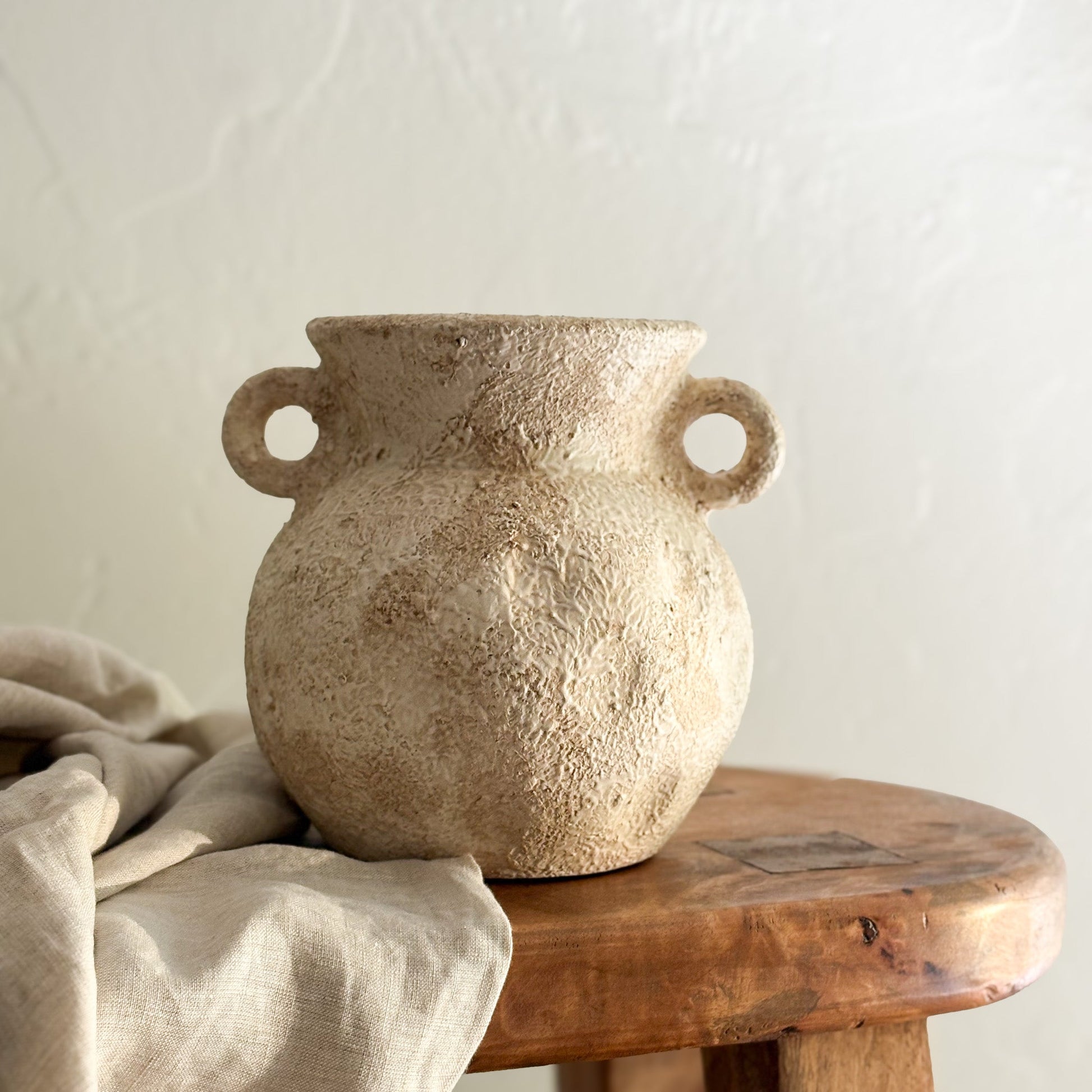Textured ceramic vase with handles on a wooden surface against a light background