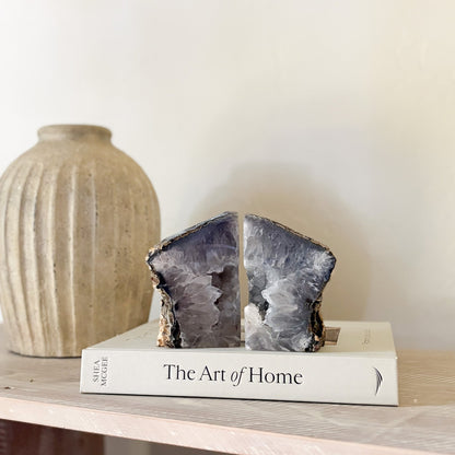 Geode bookends on a book titled 'The Art of Home' with a vase in the background.