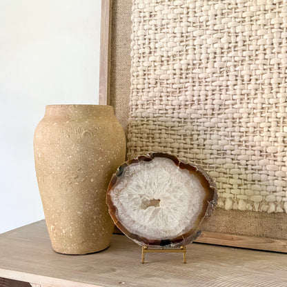 Decorative agate slice on a stand next to a textured vase against a woven wall.