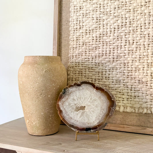 Decorative agate slice on a stand next to a textured vase against a woven wall.
