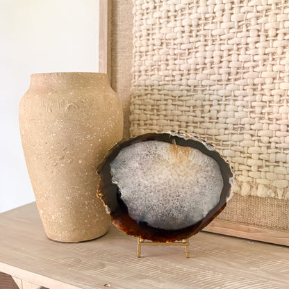 Decorative agate stone on a stand next to a textured vase against a woven wall.