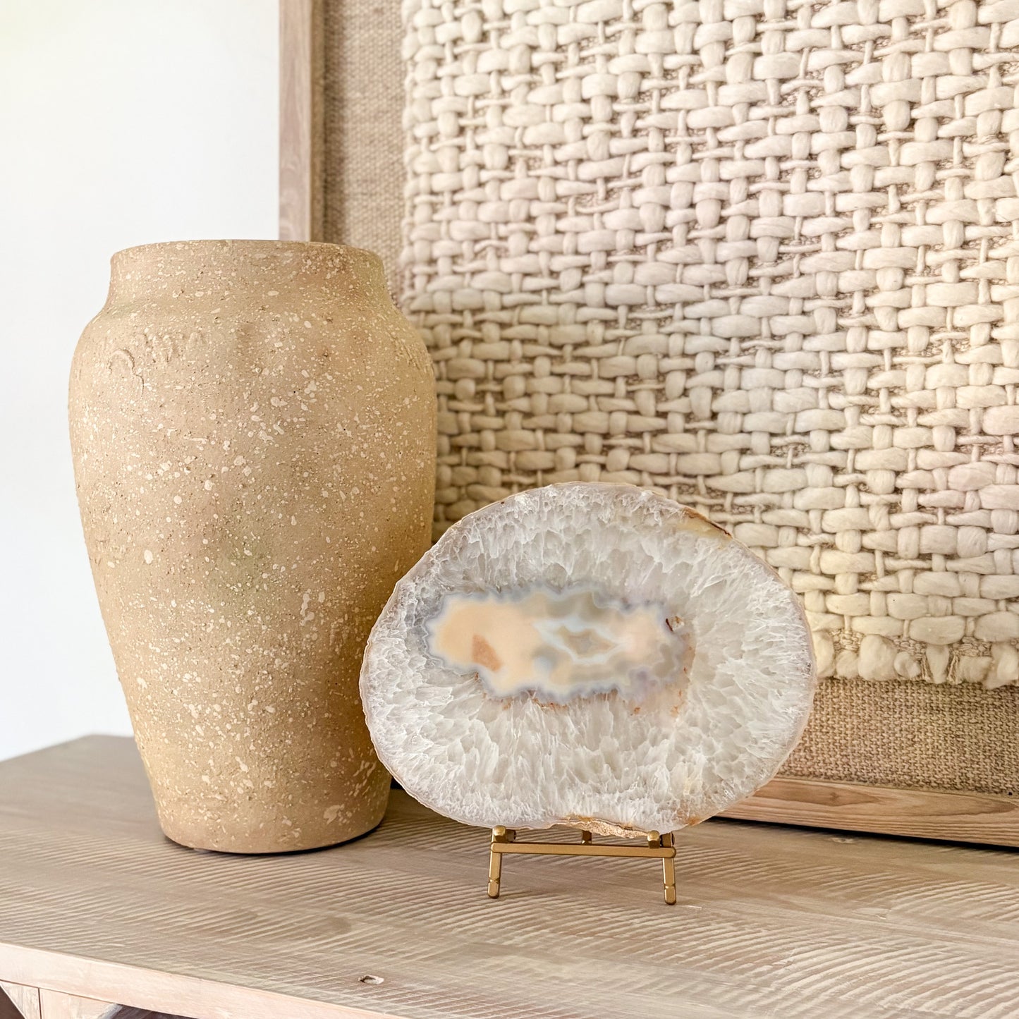 Decorative agate slab on a stand next to a textured vase against a woven wall.