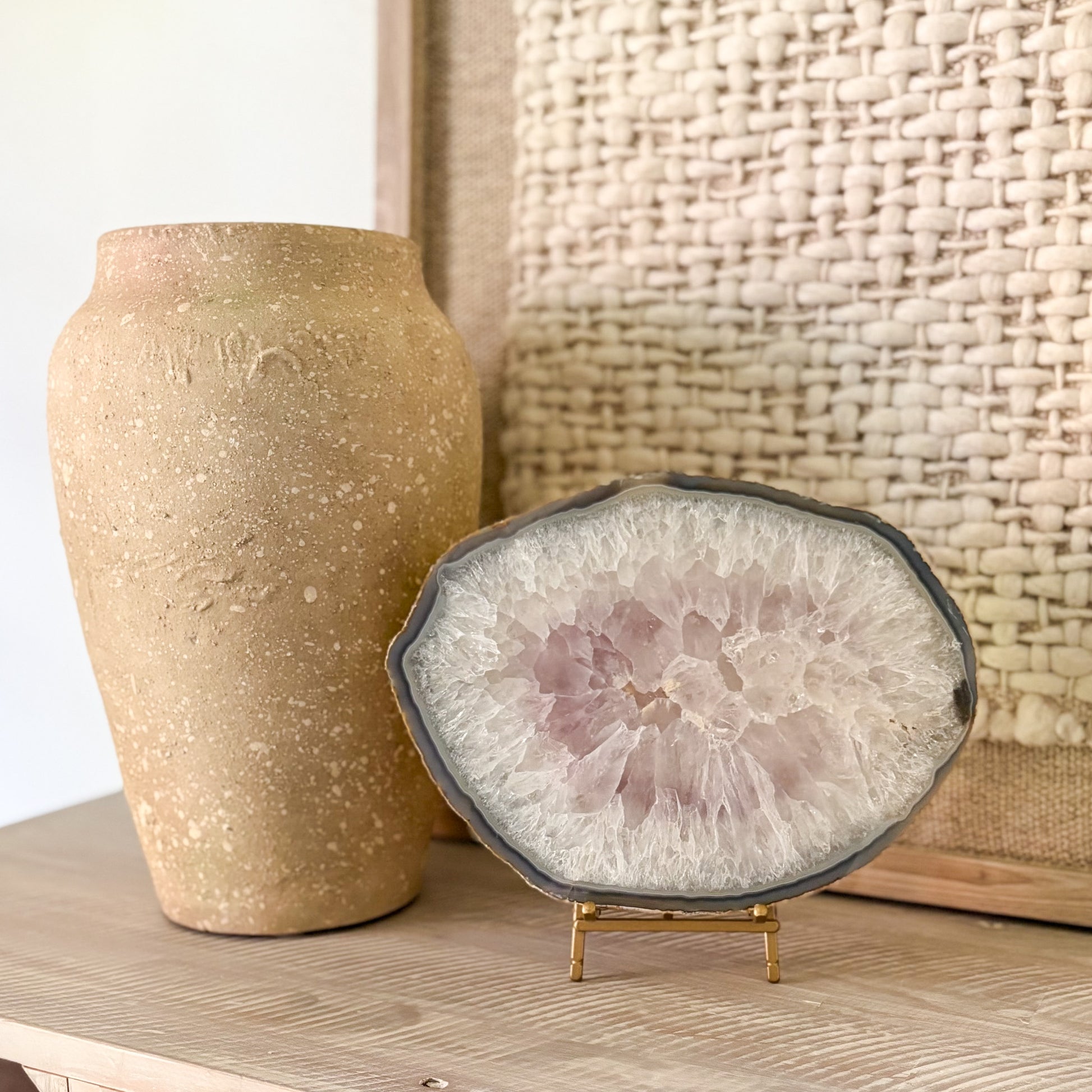Decorative agate stone slice on a stand next to a textured vase against a woven basket background