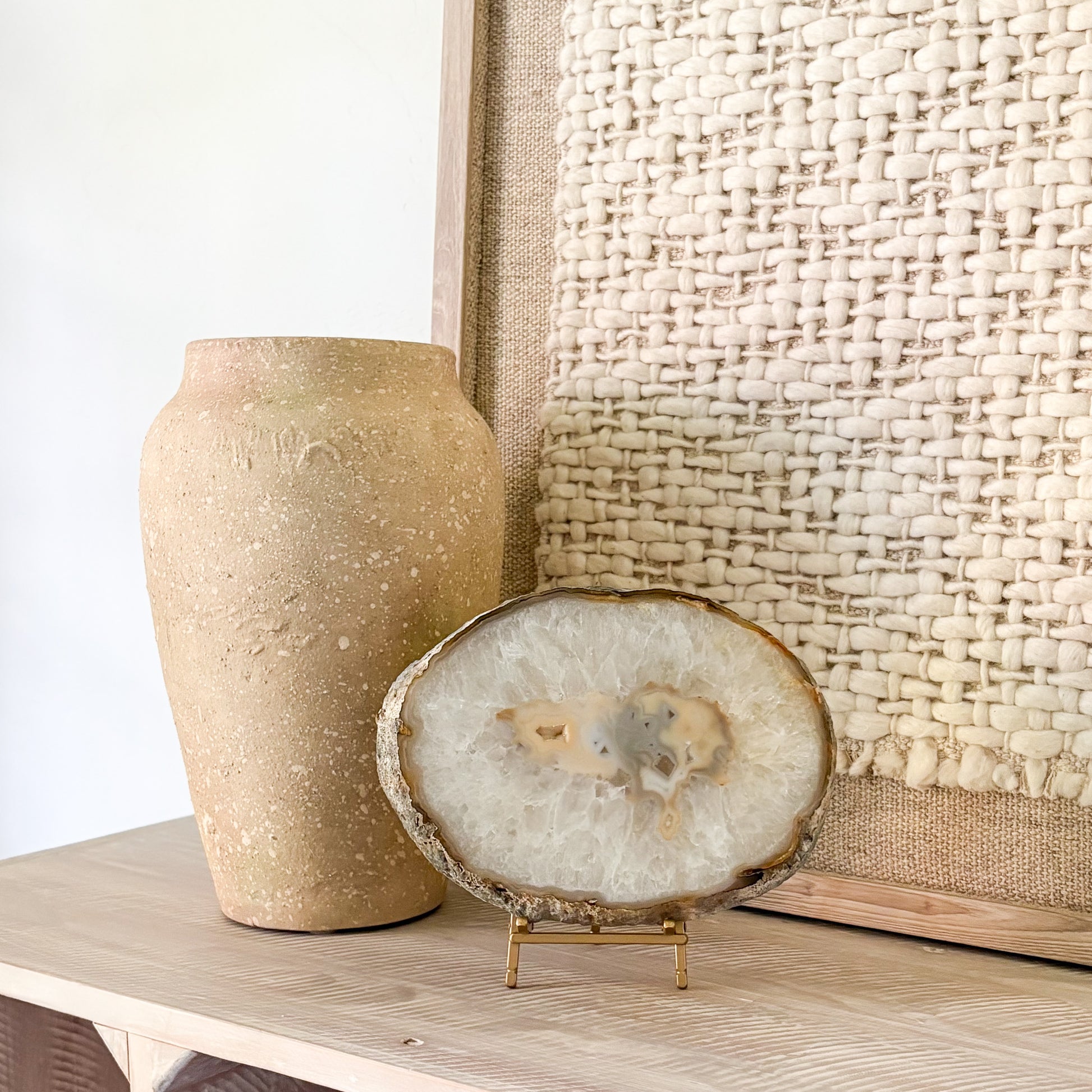 Decorative vase and sliced agate stone on a wooden surface with a textured wall in the background