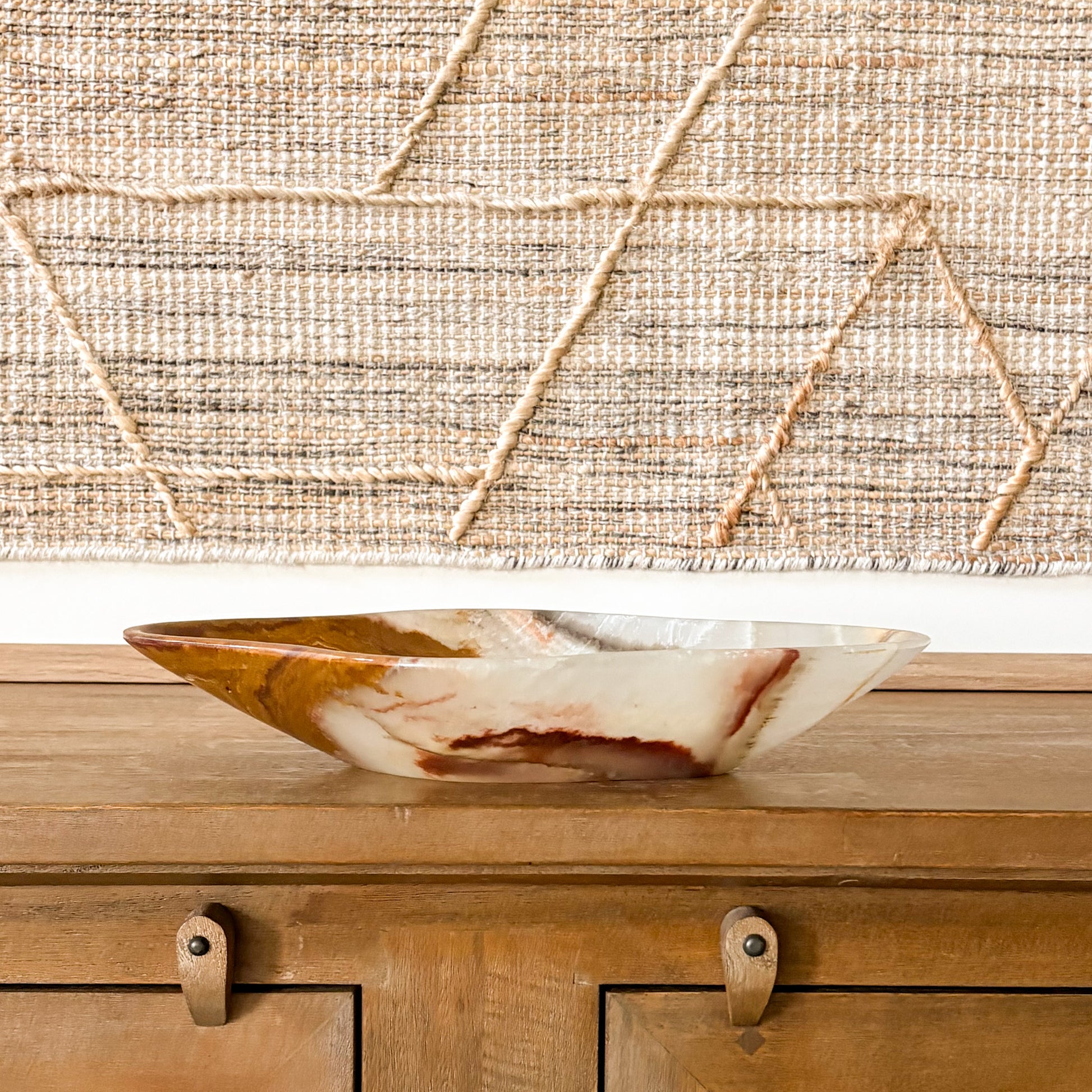 Large hand carved brown onyx bowl with natural veining, displayed on wooden console table with textured wall backdrop