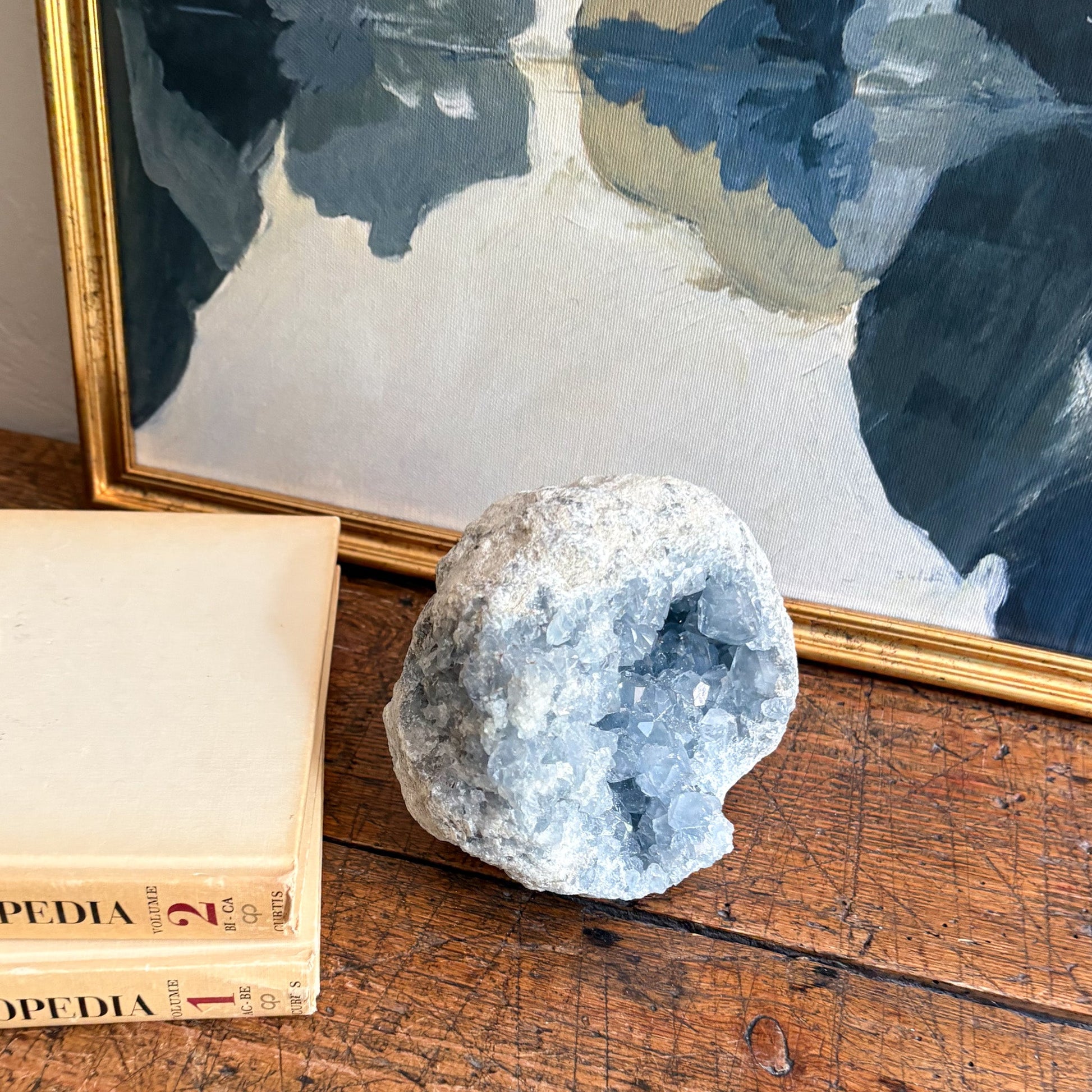 Decorative setting with a crystal geode, open book, and framed abstract art on a wooden surface.