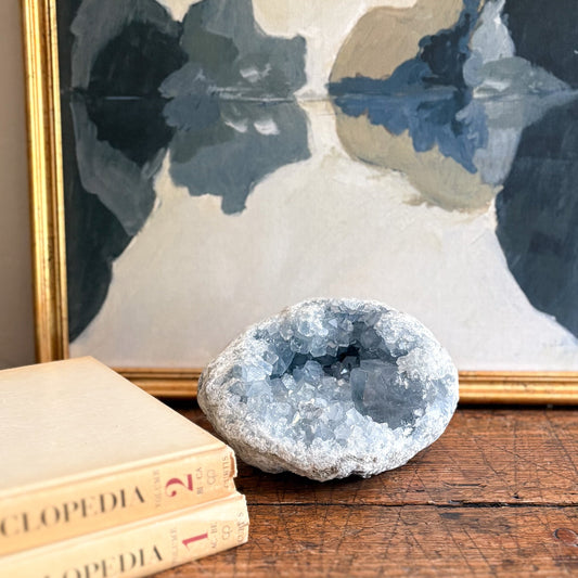 Blue Geode crystal on a wooden surface with books and a floral painting in the background