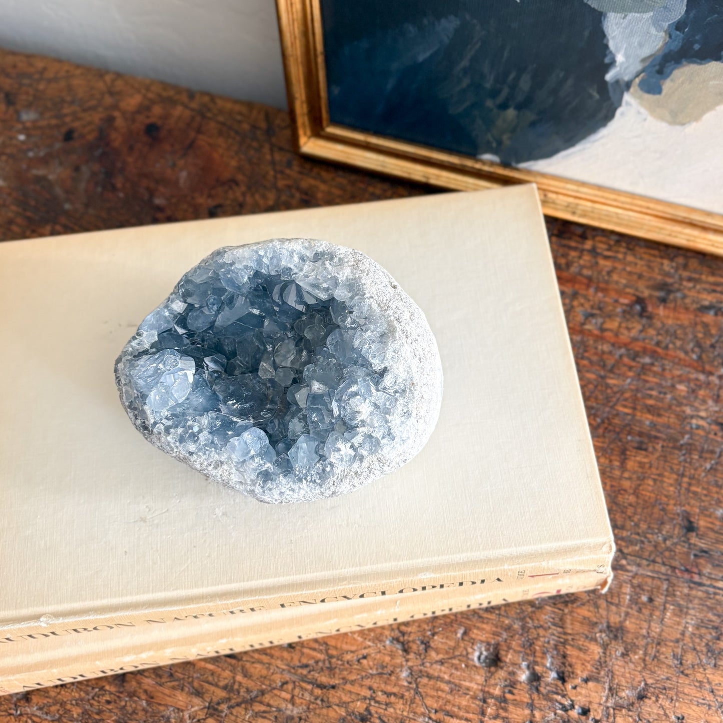 blue Geode crystal on an open book with a framed picture in the background