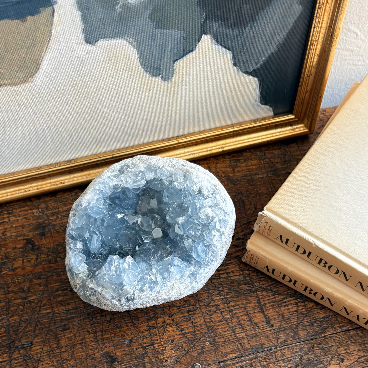 Crystal geode on a wooden surface with books and a framed picture in the background