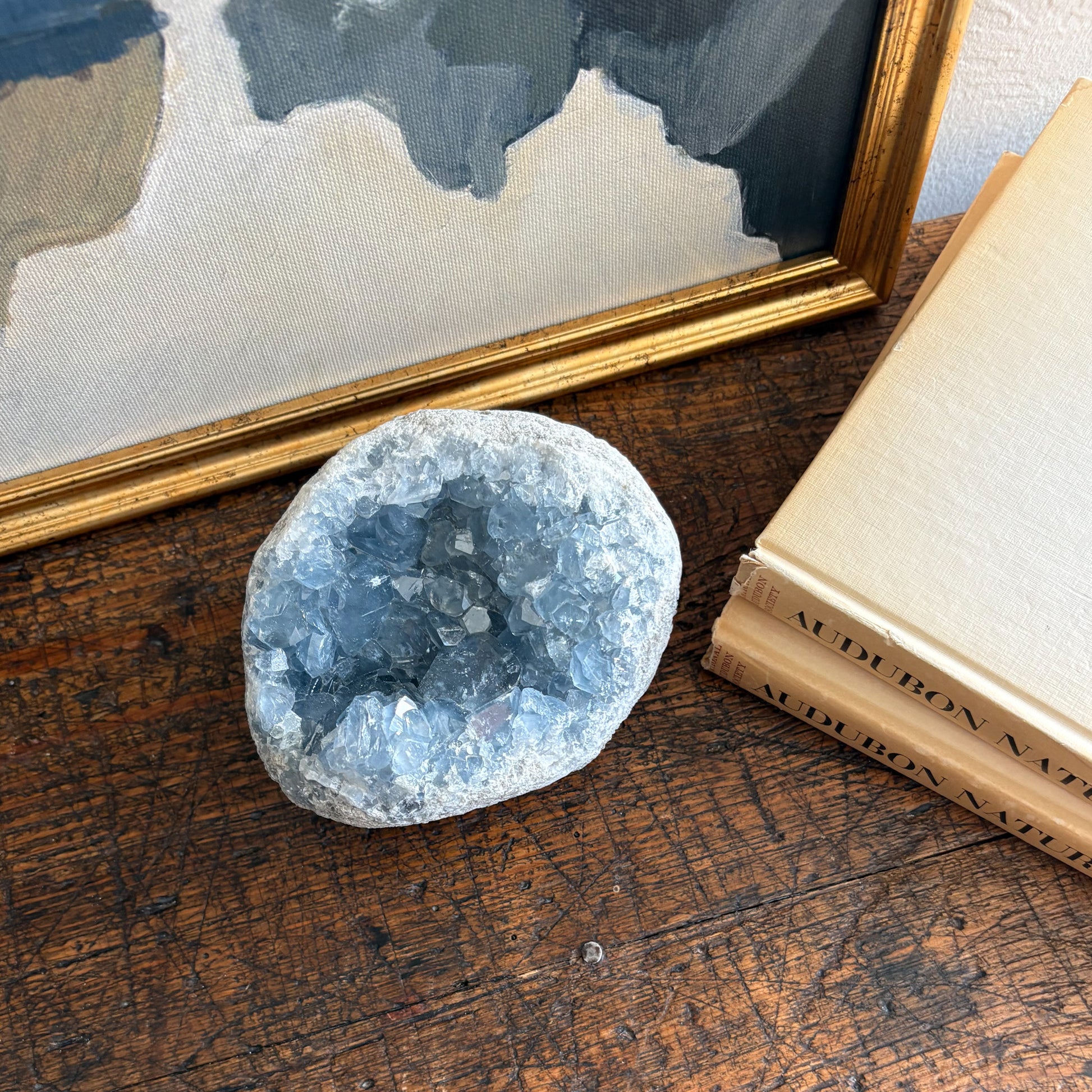 blue Geode crystal on a wooden surface with books and a framed picture in the background