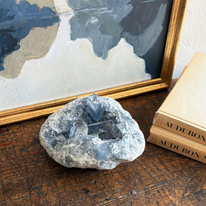 blue Crystal geode on a wooden surface with books and a framed world map in the background