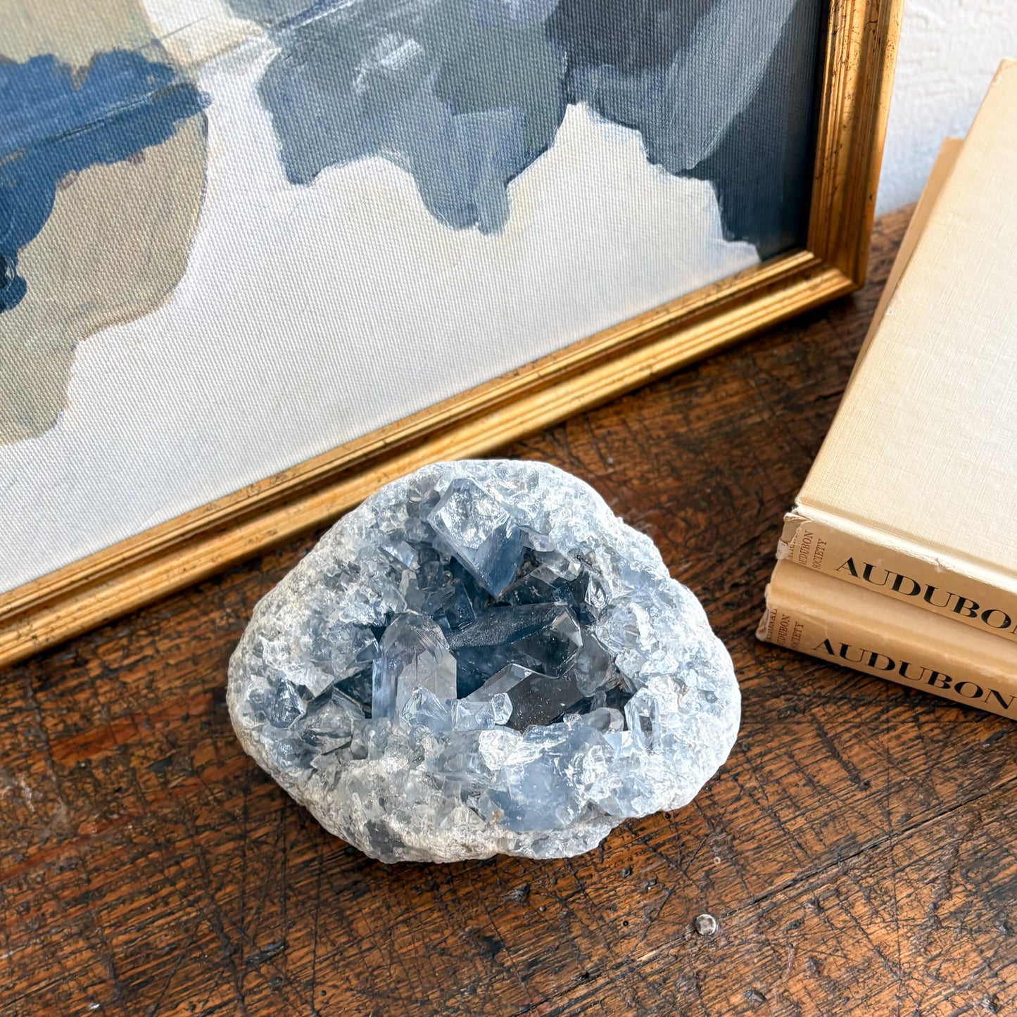 natural blue Crystal geode on a wooden surface with books and a framed picture in the background