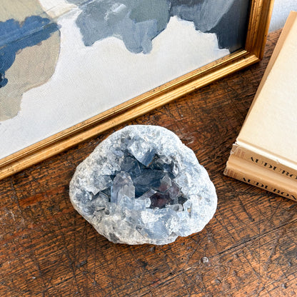 natural blue madagascar Geode crystal on a wooden surface with a framed map and book in the background
