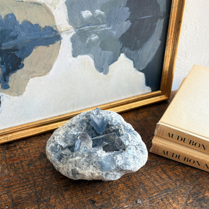 blue Crystal rock on a wooden surface with books and a framed painting in the background