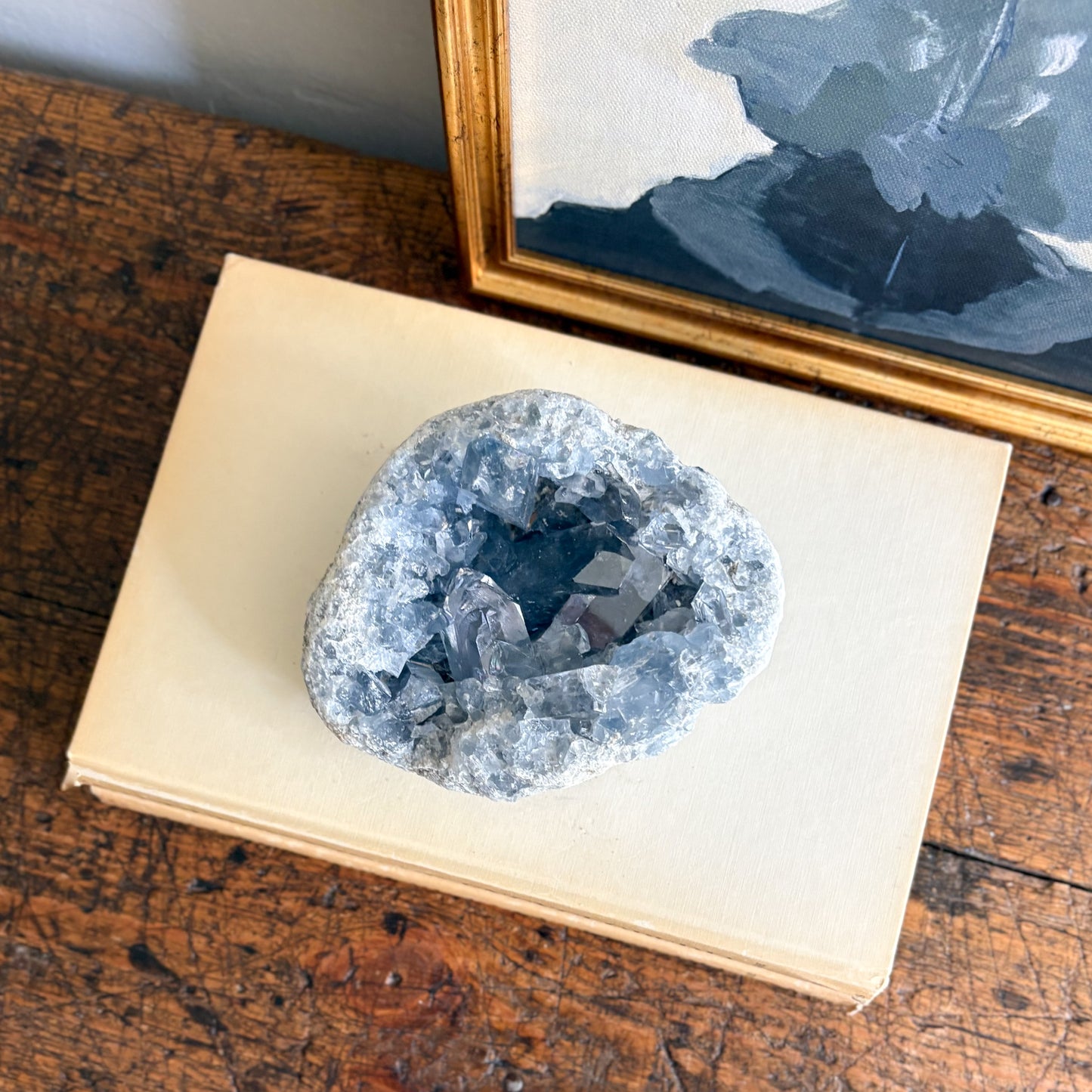 blue Geode crystal on an open book with a framed painting in the background