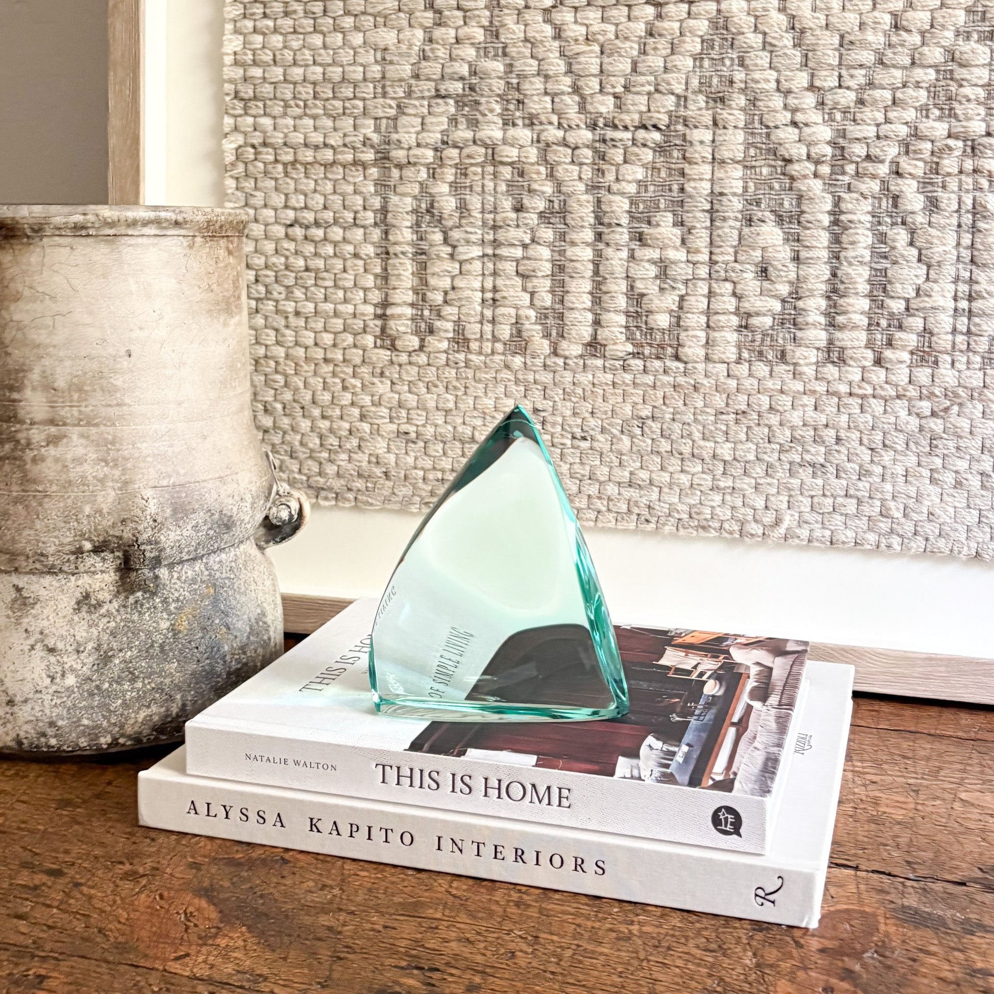 Green glass sculpture on a stack of books with a textured wall in the background