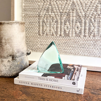 Green glass sculpture on a stack of books with a textured wall in the background