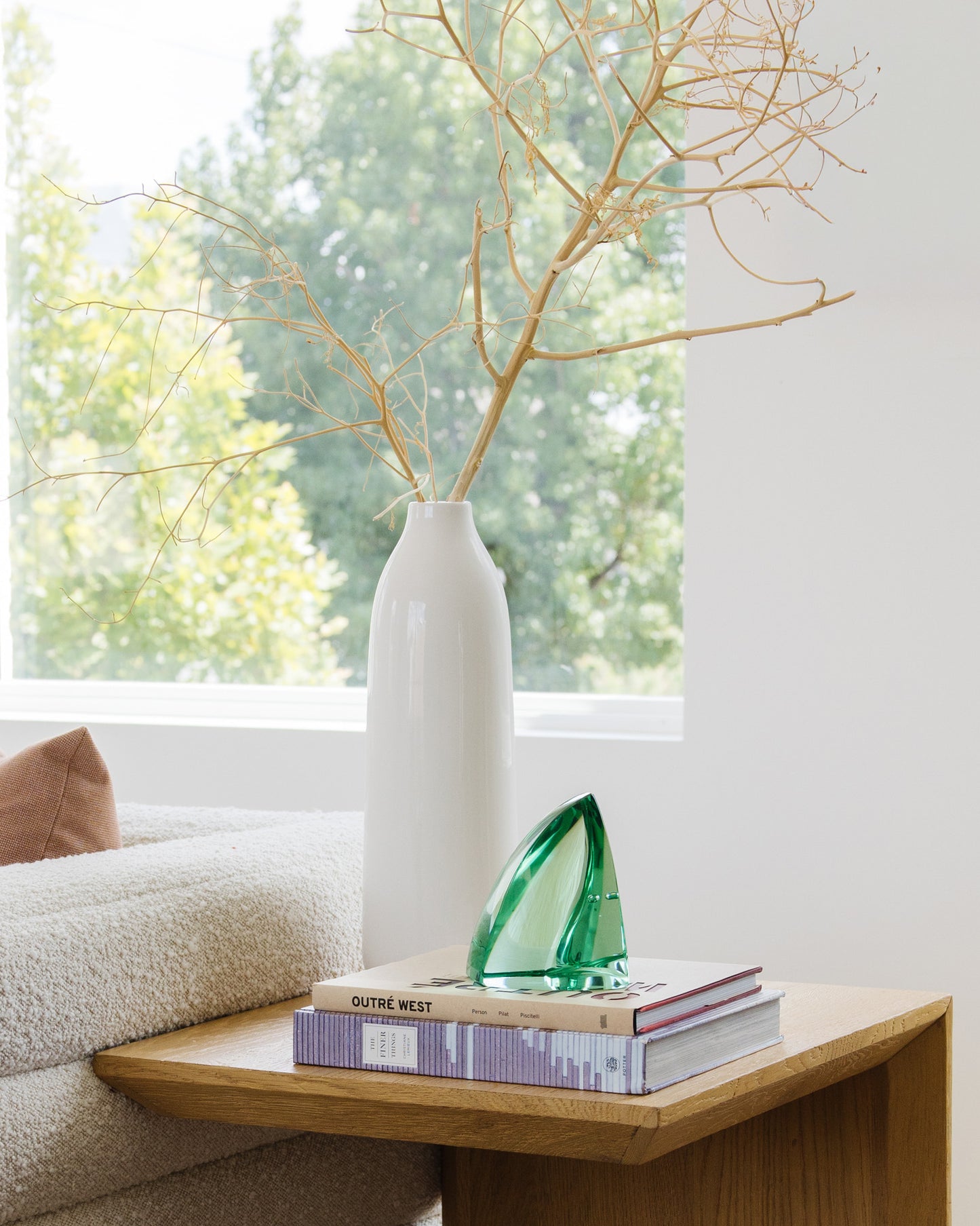 Green glass sculpture displayed on art books beside a white ceramic vase in a bright, modern living room.