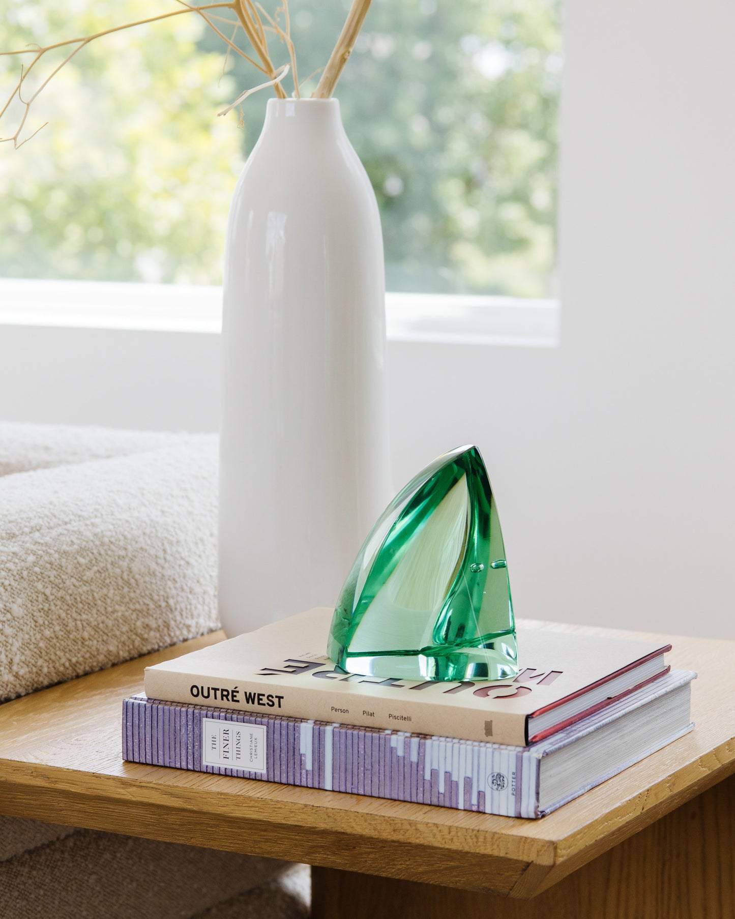 Decorative green glass sculpture on books beside a white ceramic vase