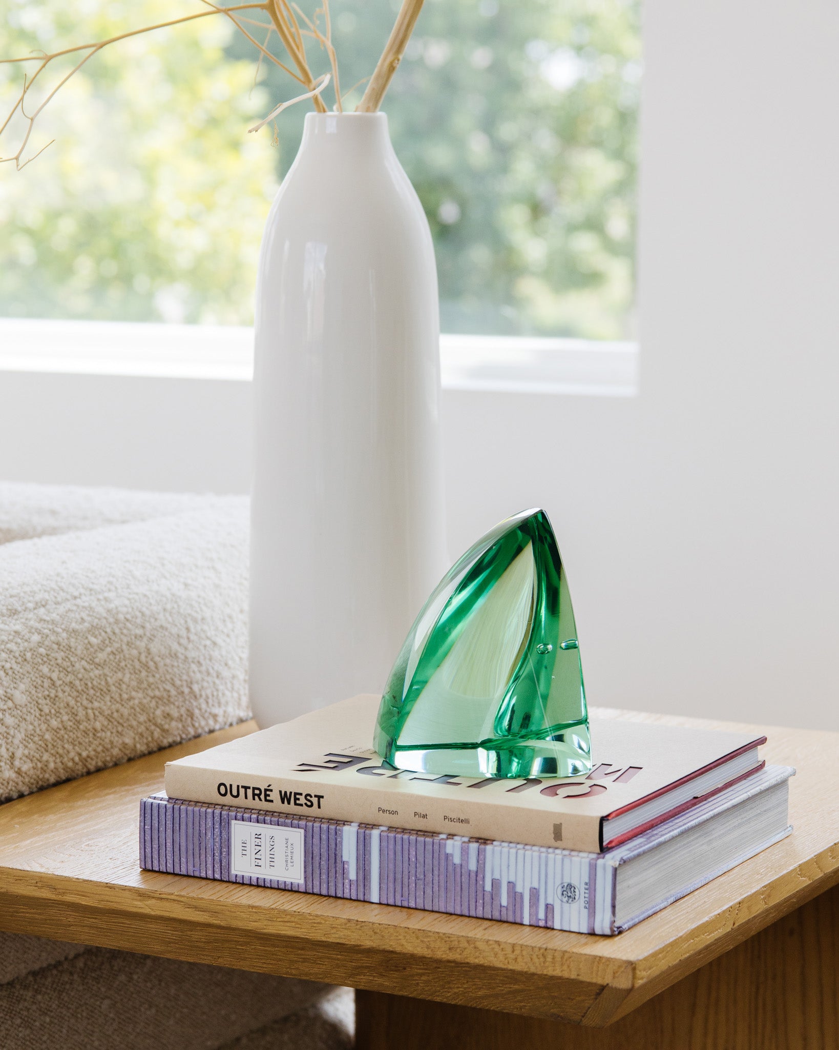 Decorative green glass sculpture on books beside a white ceramic vase