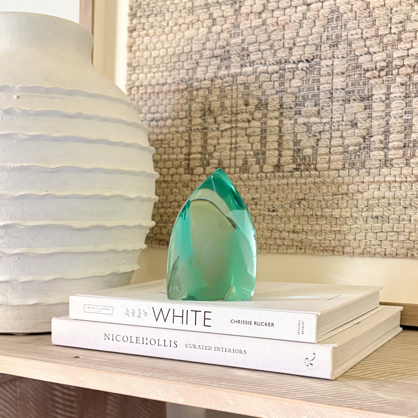 translucent green glass sculpture styled on a shelf with decor books and a ceramic vase