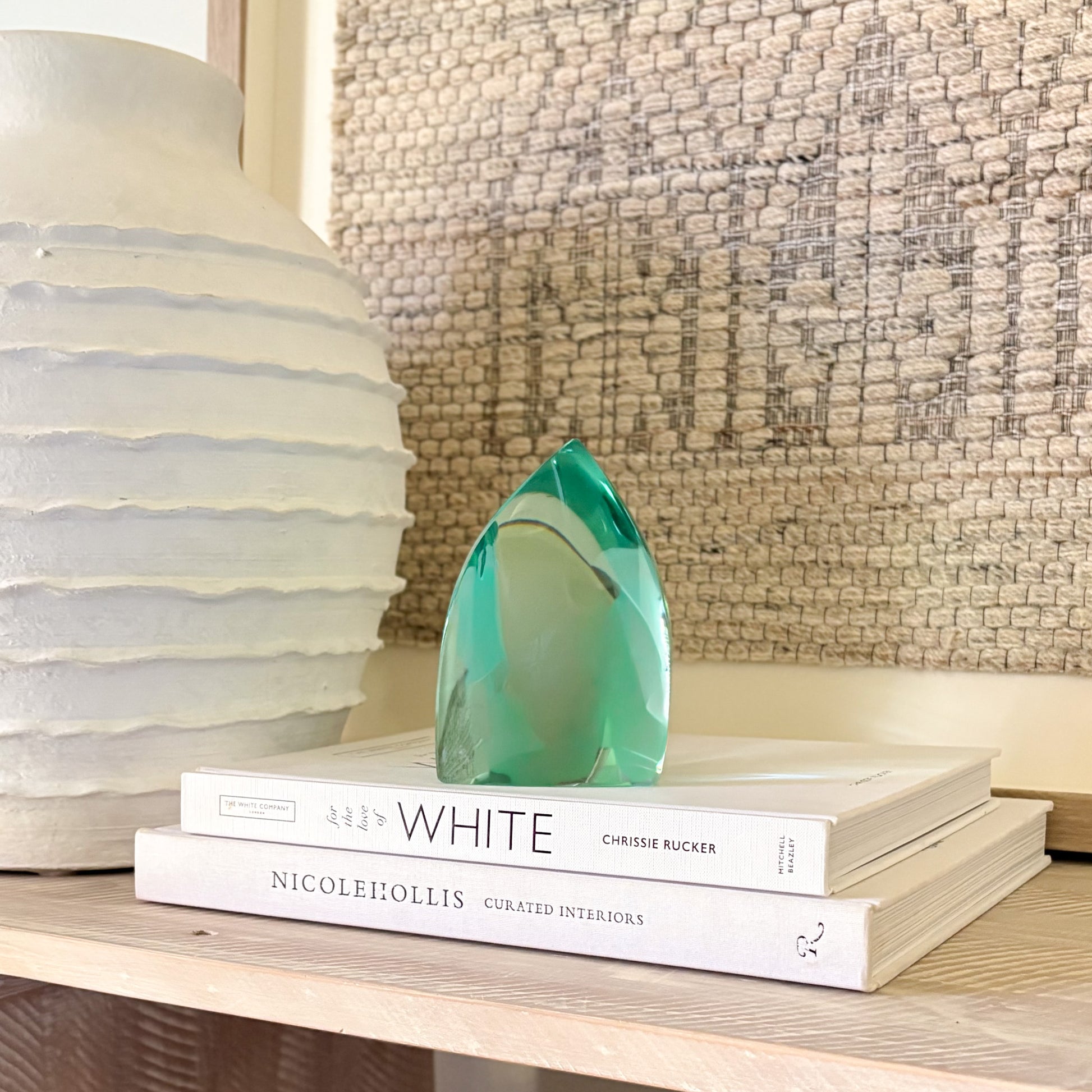 translucent green glass sculpture styled on a shelf with decor books and a ceramic vase