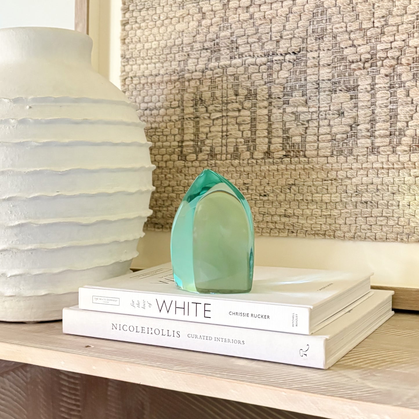 Modern green glass art piece resting on stacked interior design books beside a textured white vase