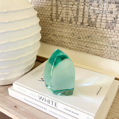 Teal glass art piece used as shelf decor in a modern, minimalist setting