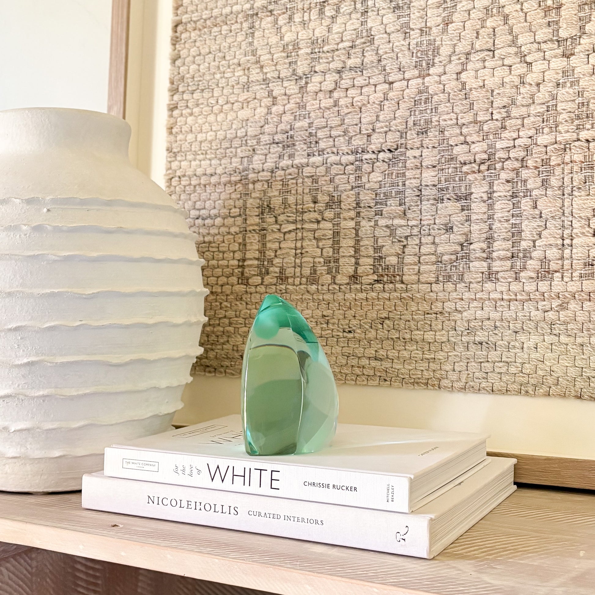 Abstract green glass sculpture with smooth, curved edges displayed on design books