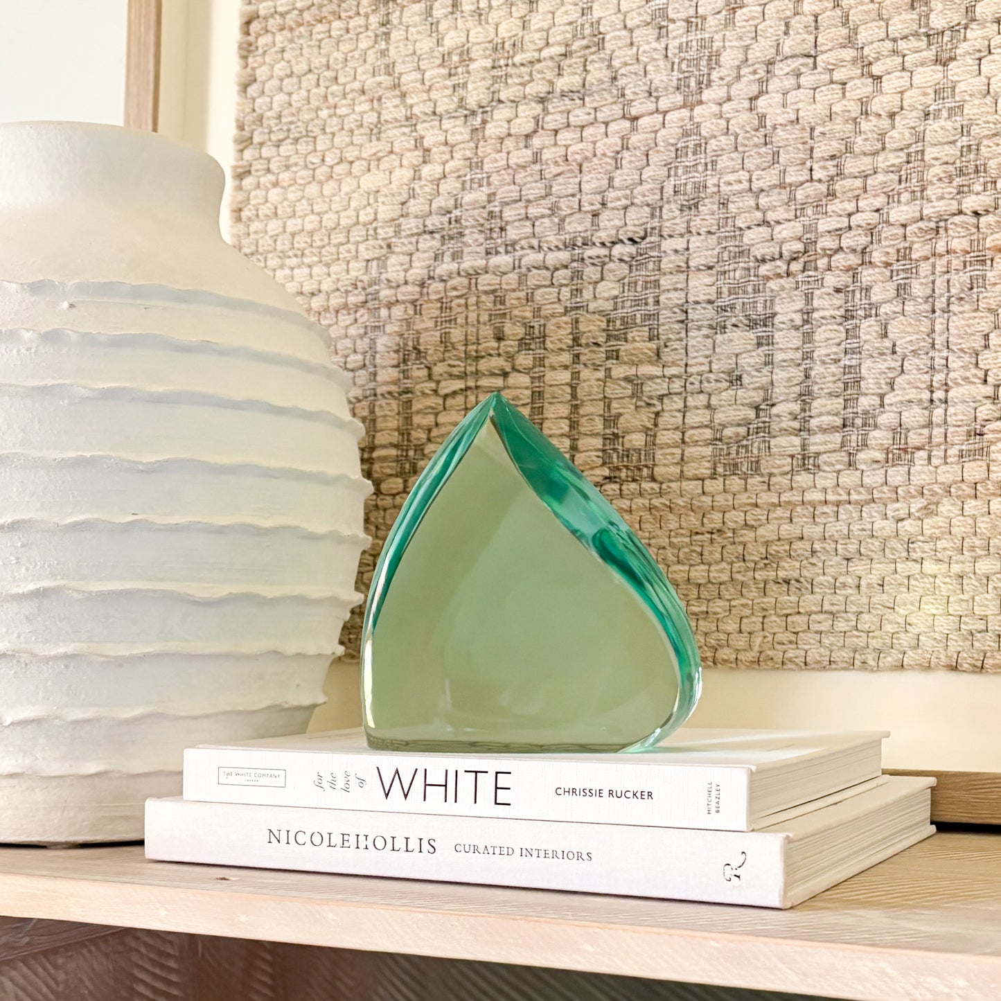Translucent green glass sculpture styled on a shelf with decor books and a ceramic vase