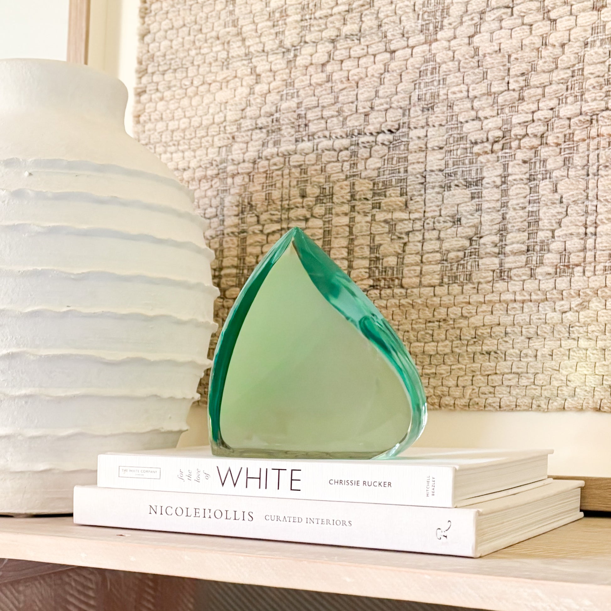 Green glass decorative sculpture styled on books beside a white textured vase in a neutral interior