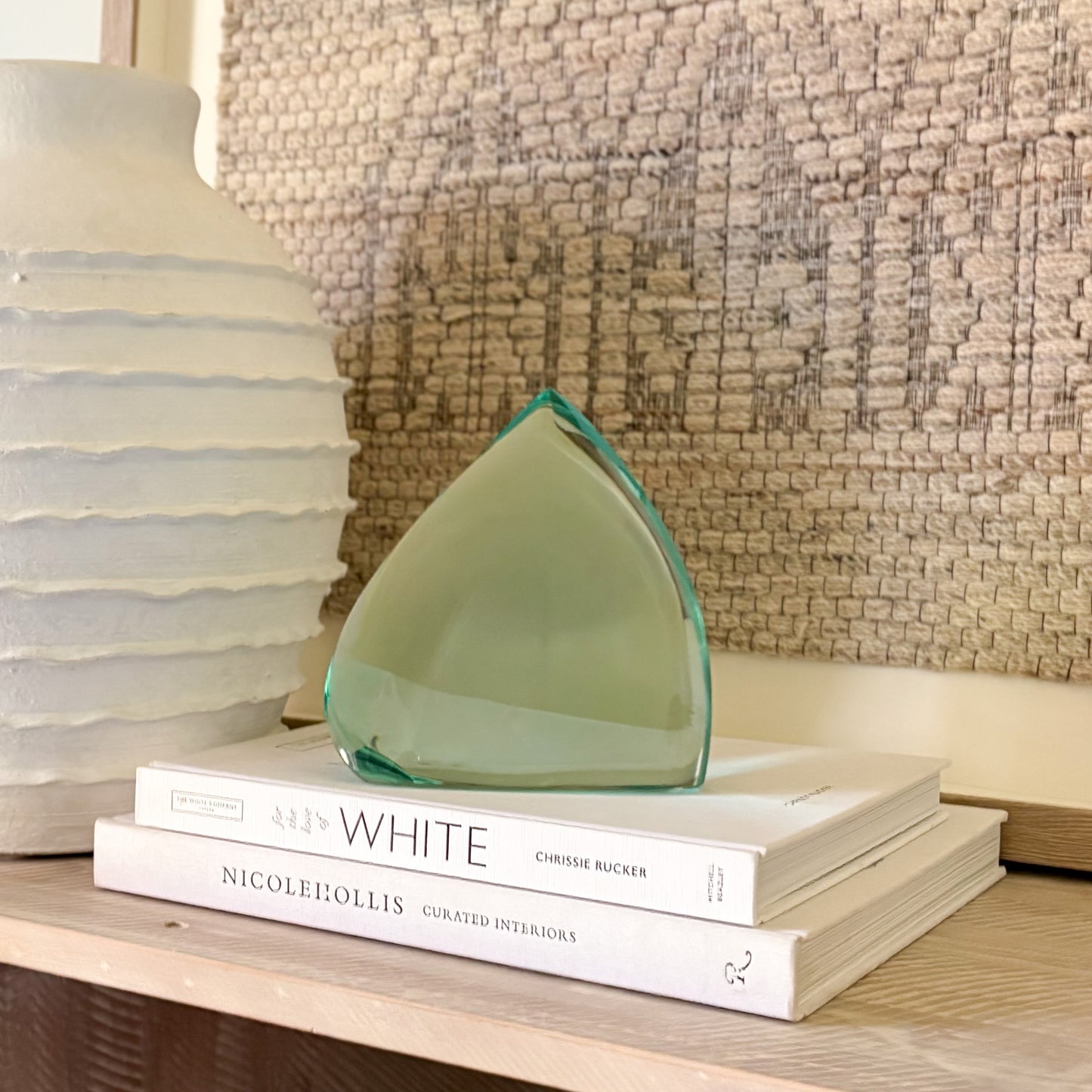 Abstract teal-green glass sculpture with polished surfaces, displayed on books for scale