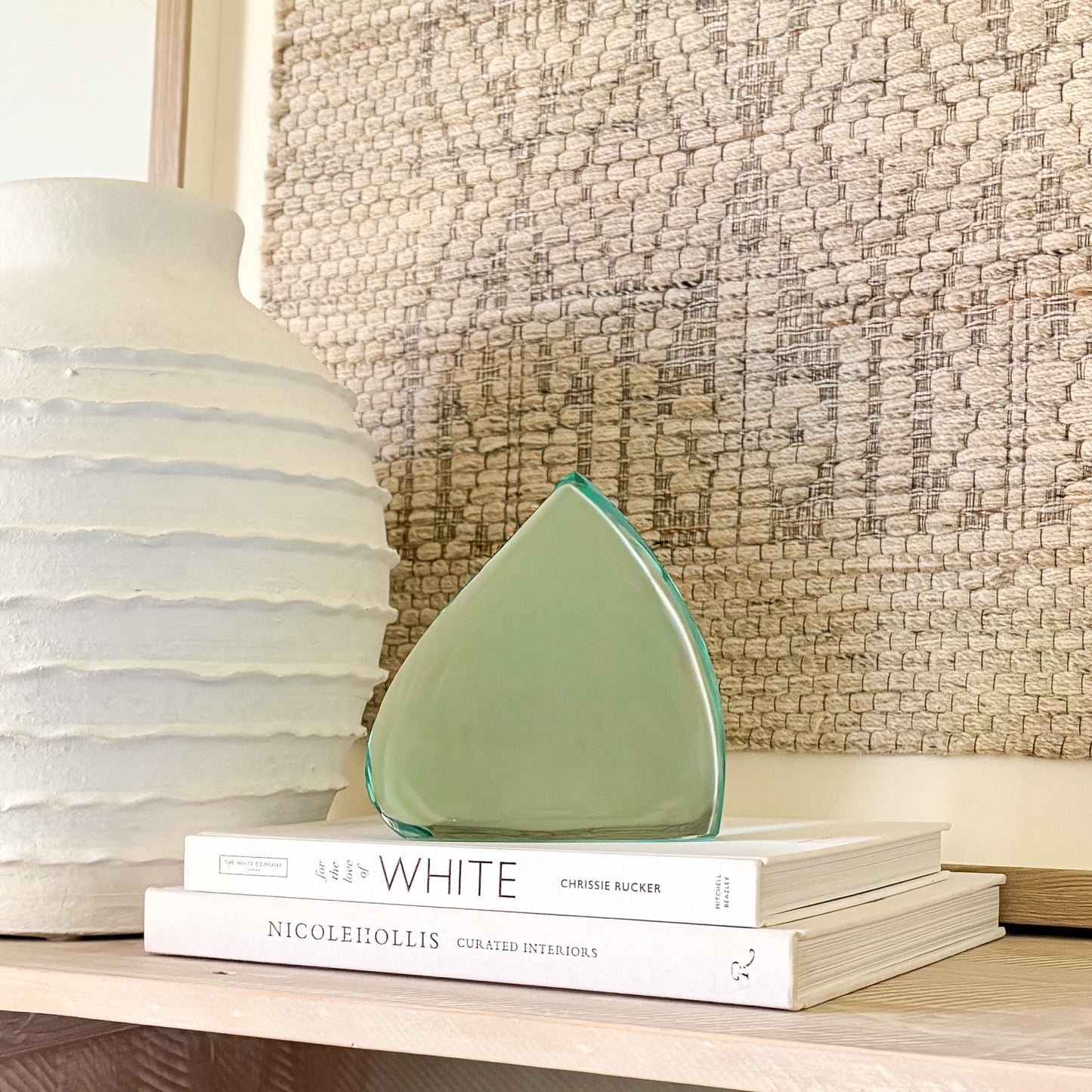 Abstract green glass sculpture with smooth, curved edges displayed on design books